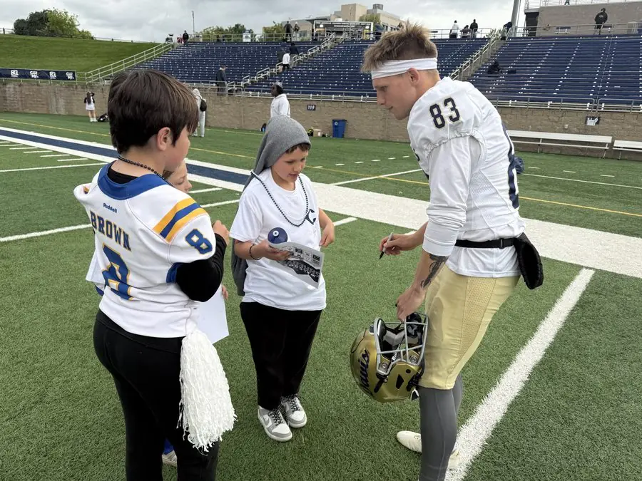 UC Davis football player signing autographs for young fans on the field